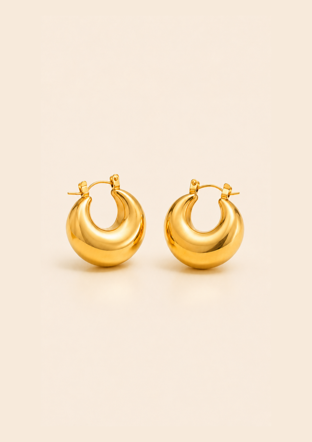 A pair of polished gold crescent-shaped hoop earrings with a smooth, reflective finish, displayed on a solid light beige background.