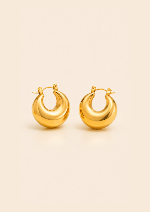 A pair of polished gold crescent-shaped hoop earrings with a smooth, reflective finish, displayed on a solid light beige background.