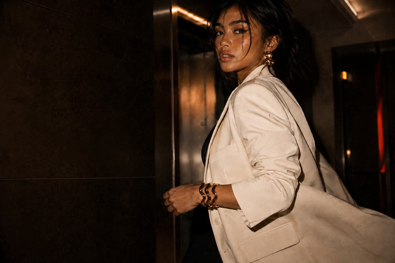 BOMBÉ model in ivory tailoring wearing sculptural gold jewelry
